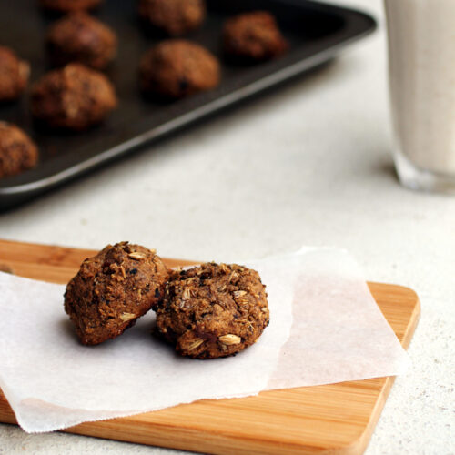 Two grainy cookies on a piece of parchment paper on a cutting board with a baking tray full of cookies in the background.