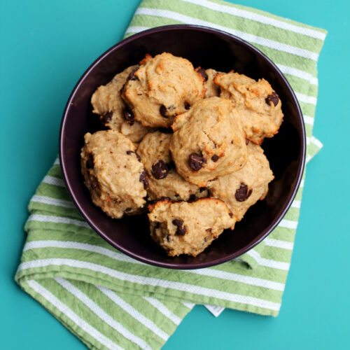 A purple bowl full of banana chocolate chip cookies on top of a green and white striped towel.