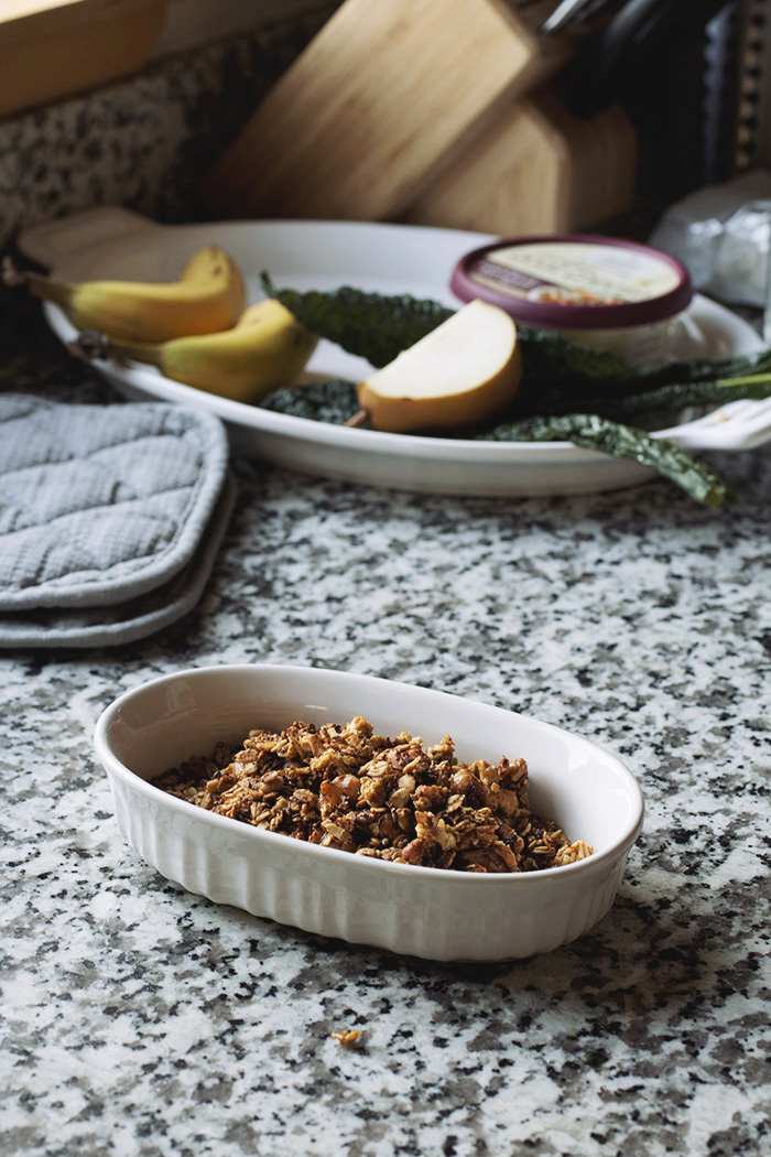 granola in a white bowl on a marble countertop with fruit in the background