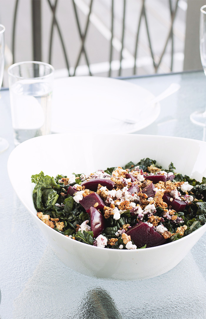 white bowl filled with kale, goat cheese, beets and walnut granola on a glass table