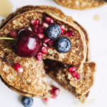 Overhead view of a stack of pancakes topped with a cherry, blueberries and pomegranate seeds.