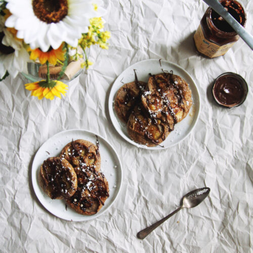 Two plates of pancakes with chocolate hazelnut spread.