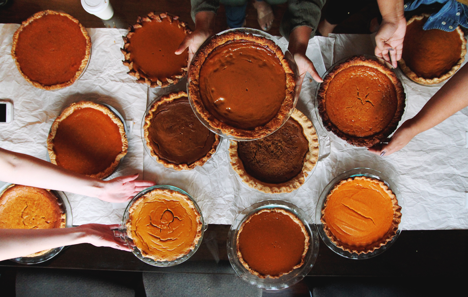 12 different recipes of pumpkin pies being passed around on white tablecloth