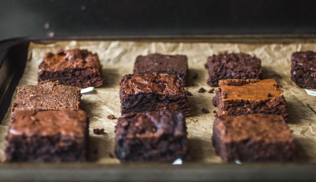 Close up on different squares of brownies on a parchment-lined baking sheet.