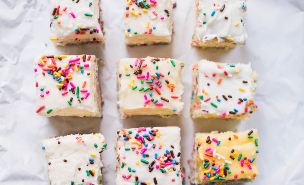 Nine slices of sprinkle cake lined up on white parchment