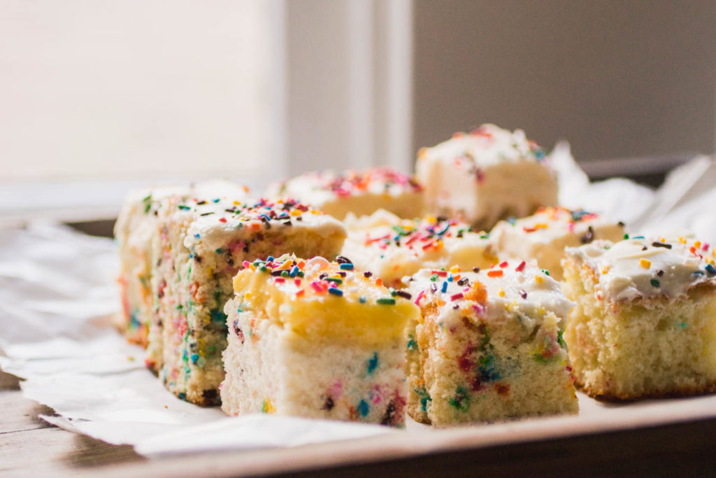 Side view of several slices of different sprinkle cake recipes on white parchment