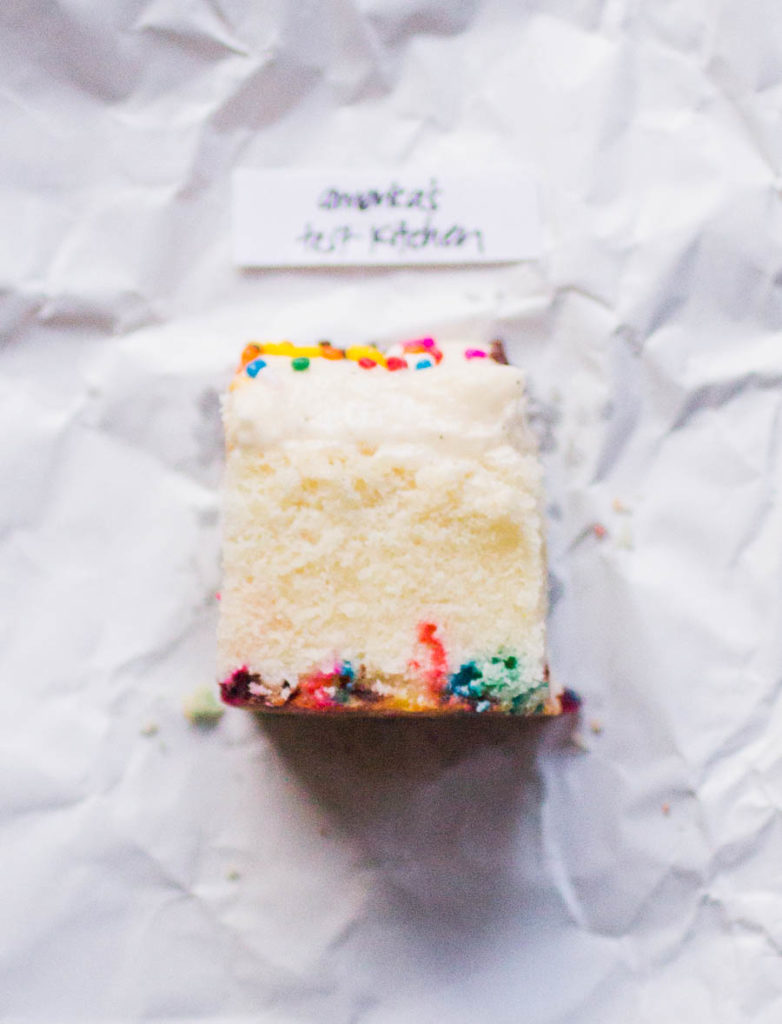 Single slice of America's Test Kitchen sprinkle cake recipe on white parchment paper