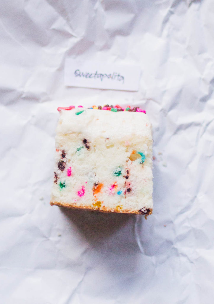 Single slice of Sweetapolita's sprinkle cake recipe on white parchment paper