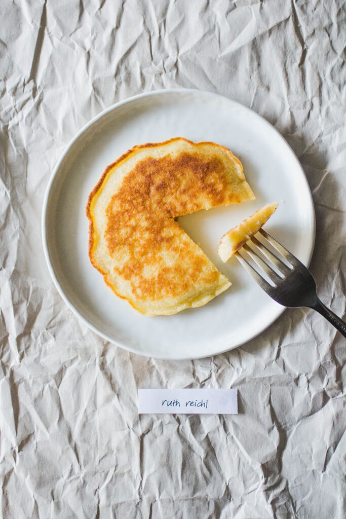 Ruth Reichl pancake with a bite out of it, sitting on a white plate.