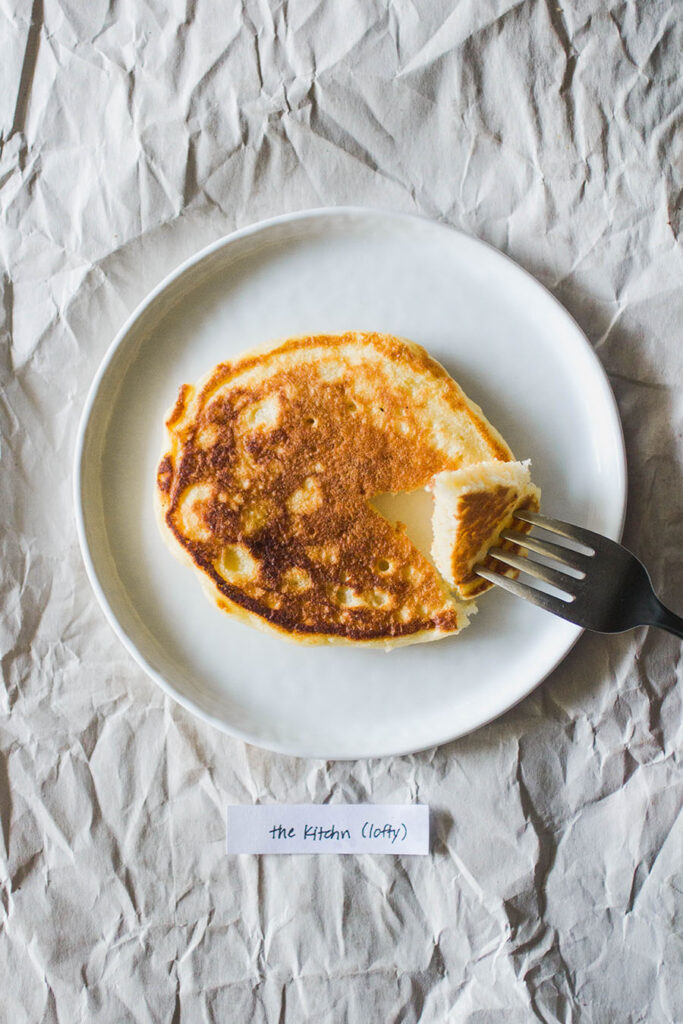 pancake on a white plate with a "the kitchn (lofty)" label with a fork taking a bite.