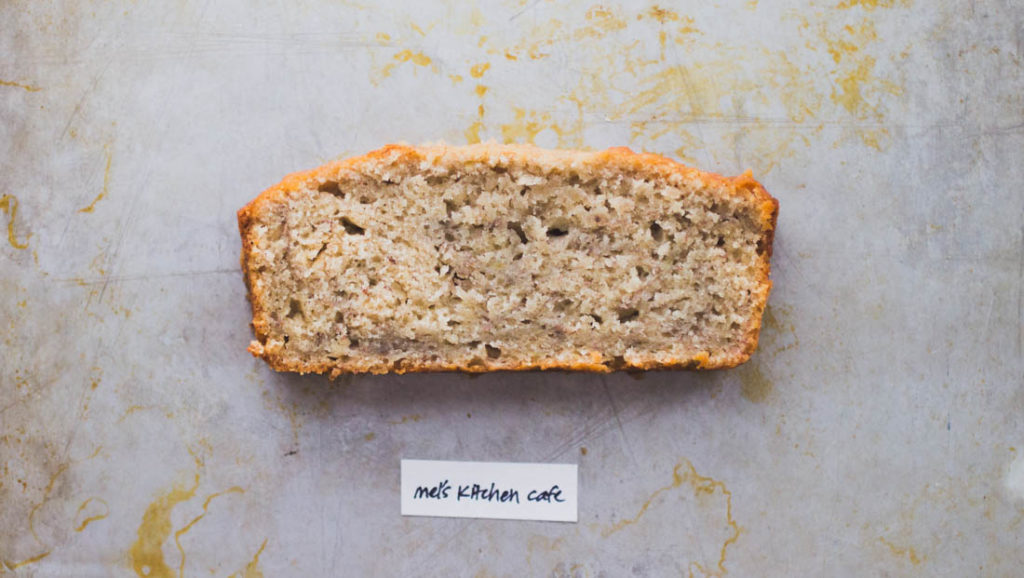 Short slice of dense golden colored cream cheese banana bread on baking tray - Recipe by Mel's Kitchen Cafe