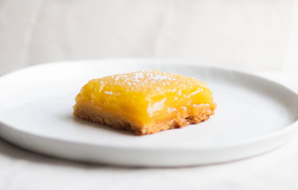 Single slice of new york times lemon bars on white plate made with olive oil and sea salt