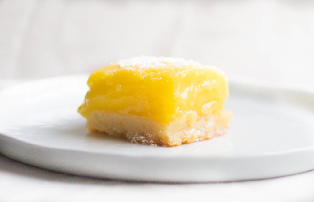 Single slice of flour bakery lemon bar with bright yellow lemon curd on a white plate