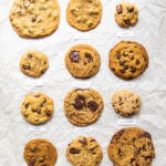 12 different vegan chocolate chip cookie recipes lined up on parchment paper