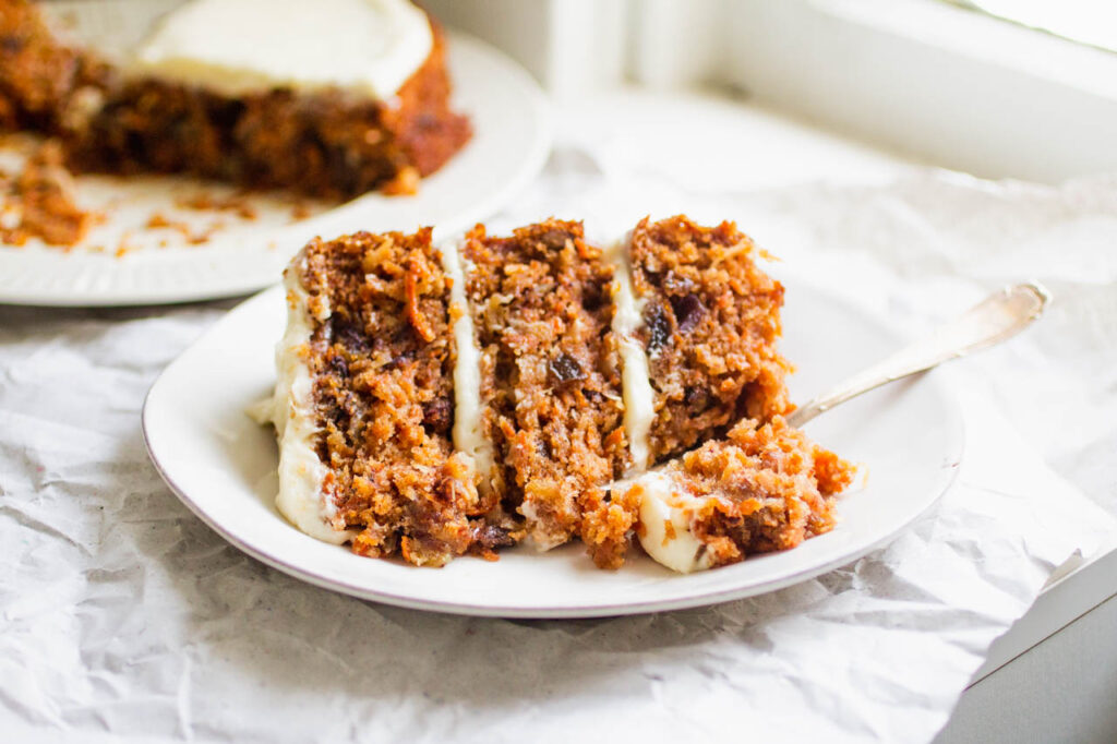a slice of three layer carrot cake on a white plate with a fork.