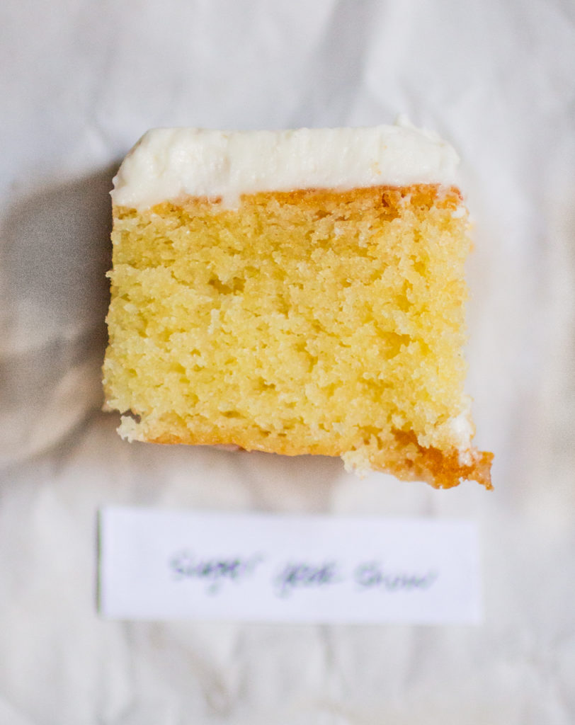 rectangular chunk of yellow cake with white frosting on a white paper background