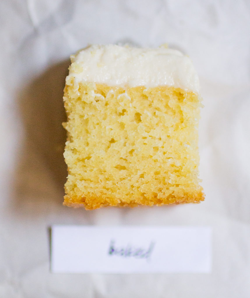 square piece of yellow cake with white frosting on a white paper background
