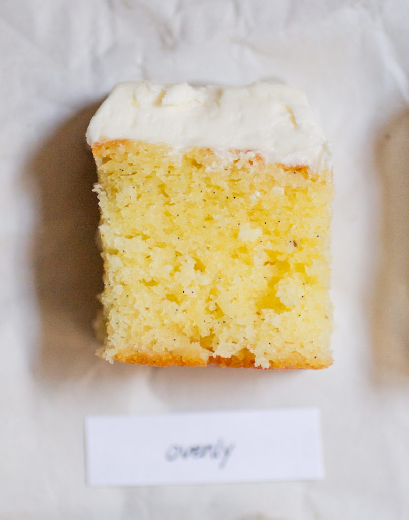 rectangular chunk of yellow cake with white frosting on a white paper background