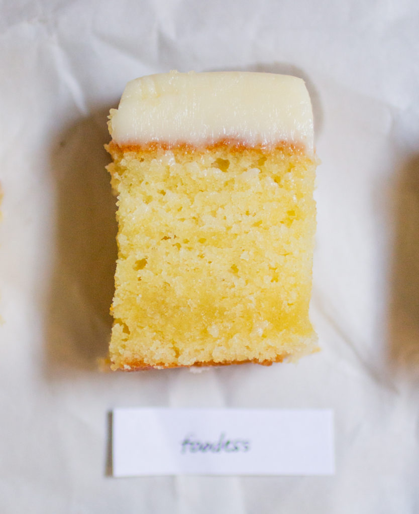 rectangular chunk of yellow cake with white frosting on a white paper background