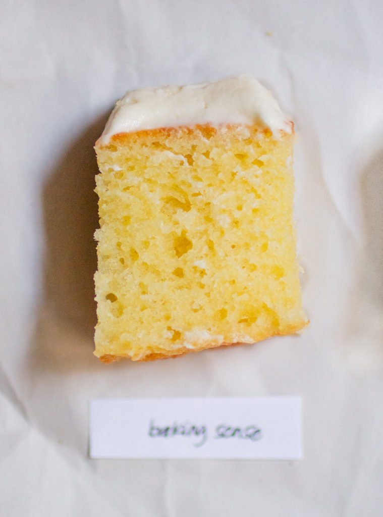 rectangular chunk of yellow cake with white frosting on a white paper background