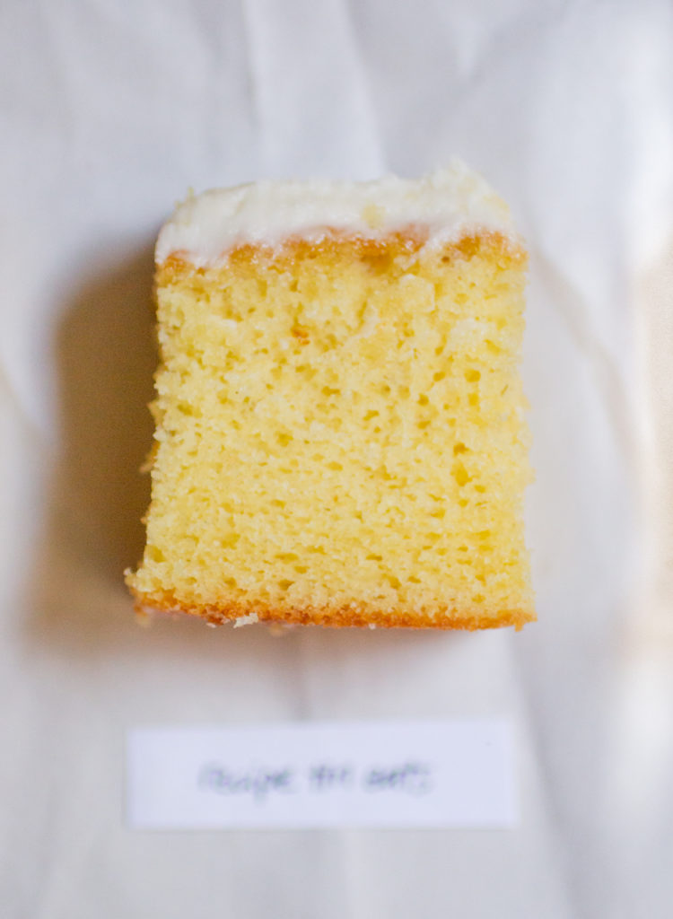rectangular chunk of yellow cake with white frosting on a white paper background