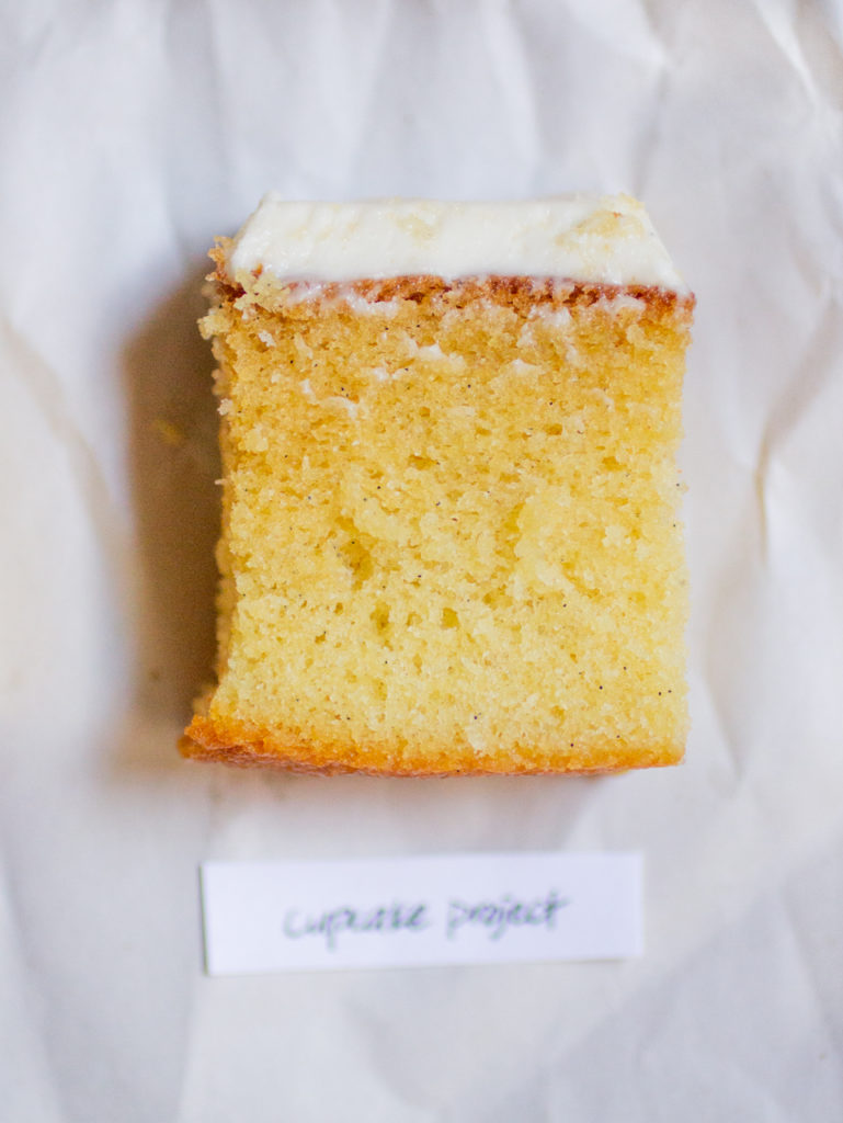 rectangular chunk of yellow cake with white frosting on a white paper background