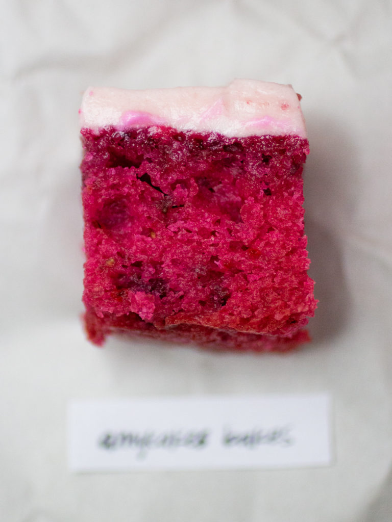 slice of fuchsia colored strawberry cake topped with light pink icing by Amycakes Bakes