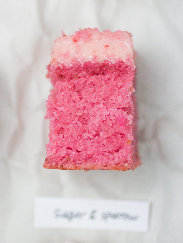 Slice of pink strawberry cake from Sugar and Sparrow on white parchment paper