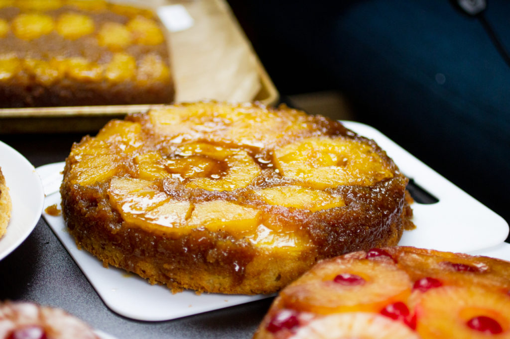 a whole pineapple upside down cake on a white cutting board near other cakes