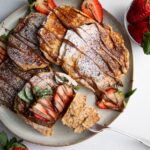 a plate of pancakes drizzled with nutella and strawberries.
