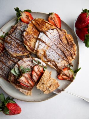 a plate of pancakes drizzled with nutella and strawberries