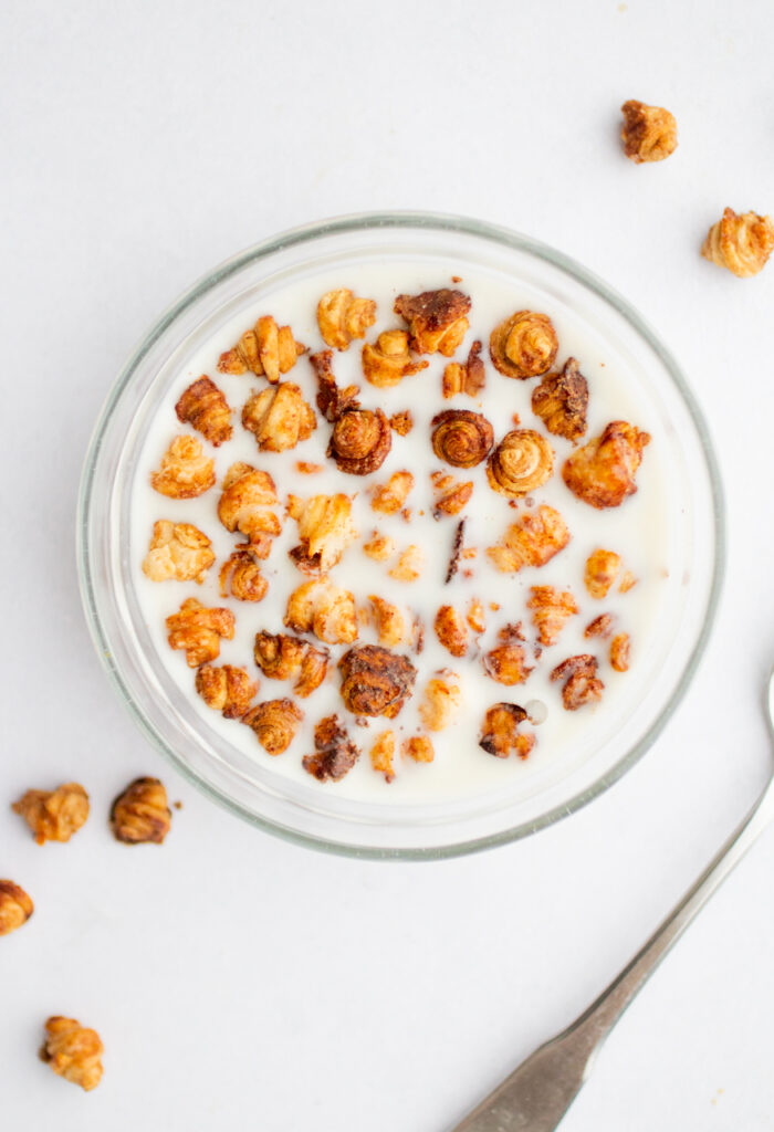 A glass bowl filled with mini croissant cereal and milk.