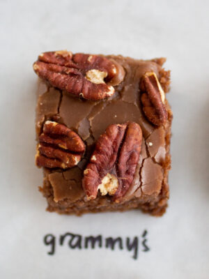 a square of chocolate cake with pecans on a white background