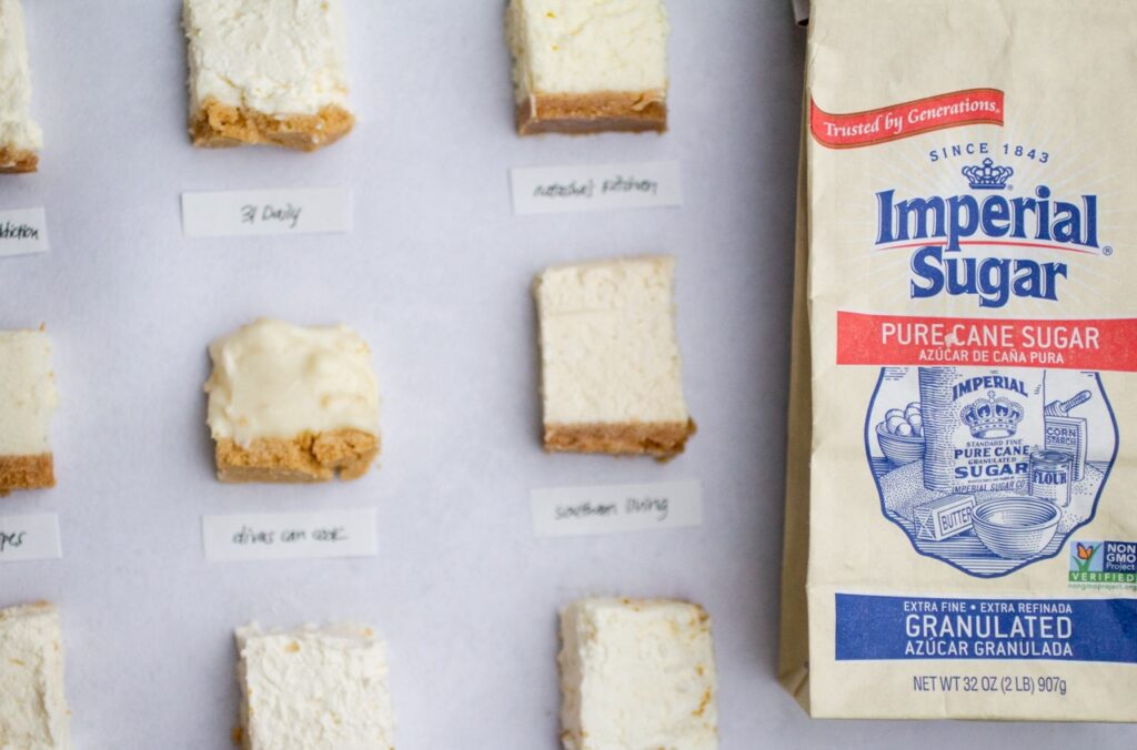 squares of cheesecake on a gray background with a bag of imperial sugar.