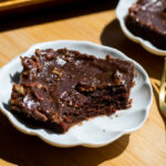 A slice of chocolate cake topped with chocolate frosting and pecans.