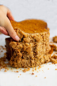 a hand picking up a slice of pumpkin bread on a white background