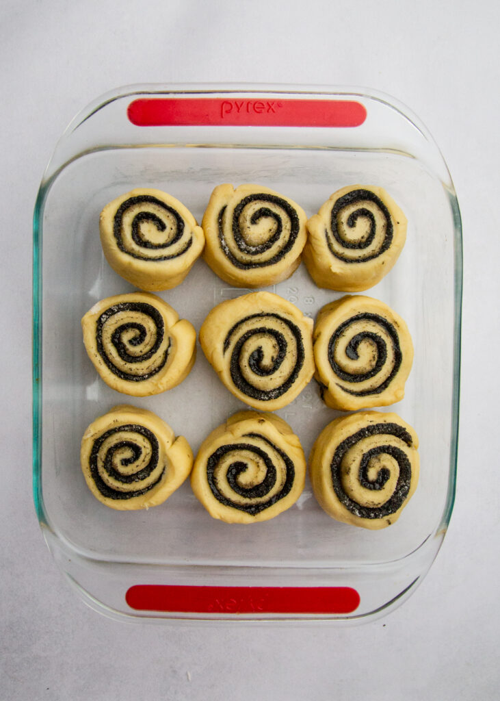 9 black sesame sweet rolls rising in a square glass pan