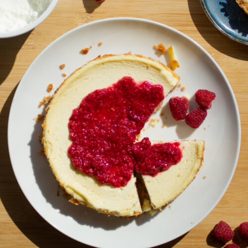 A cheesecake topped with a raspberry compote with a slice missing on a white plate.