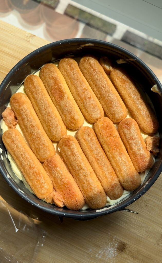 Ladyfingers laid over mascarpone cream in a pan.