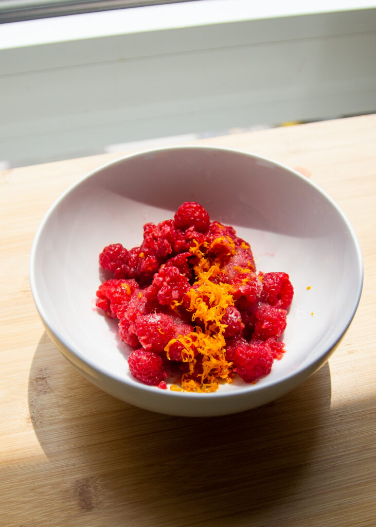 Raspberries and orange zest in a white bowl.
