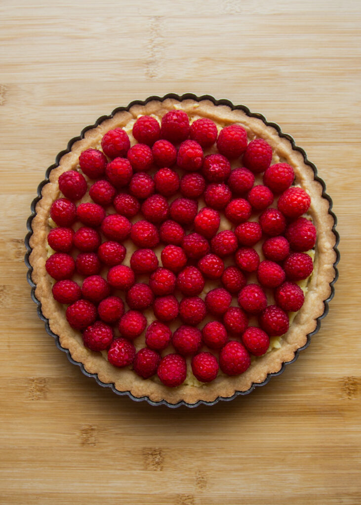 A baked tart shell filled with custard and whole raspberries.