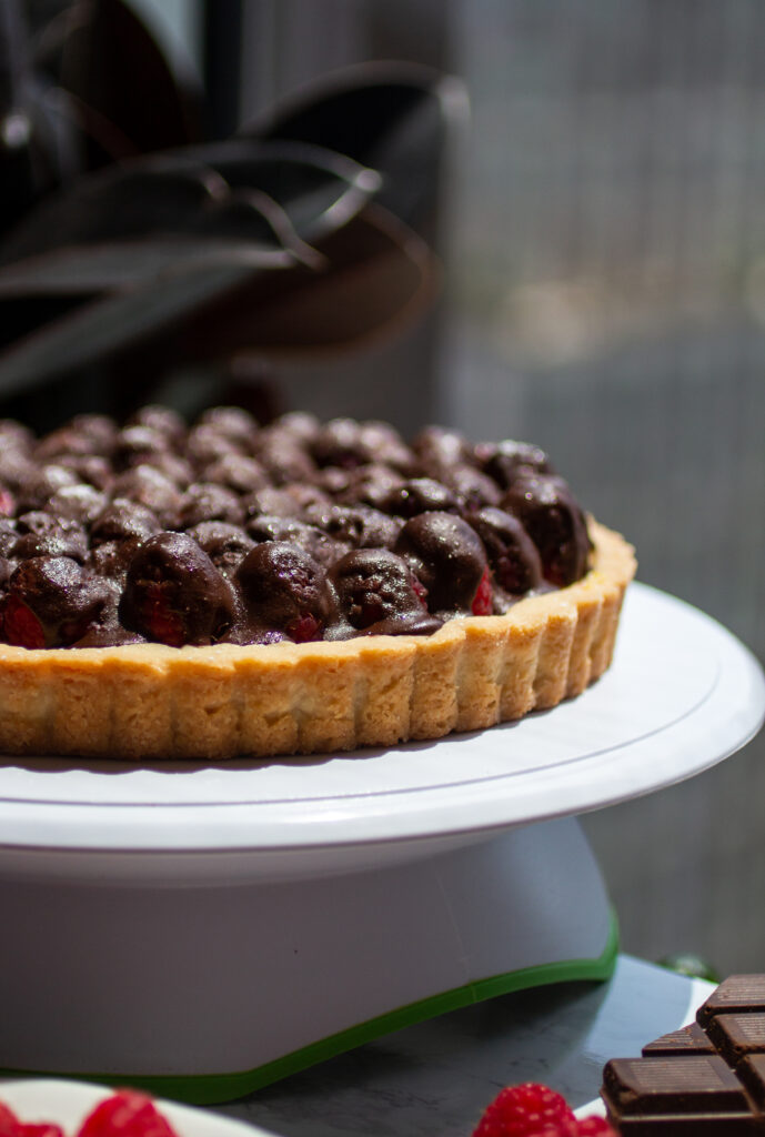 A side view of a chocolate raspberry tart on a white platter.