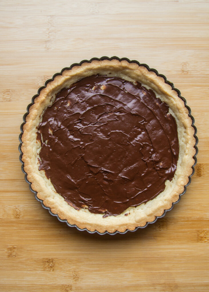 A baked tart shell with chocolate spread across the bottom.