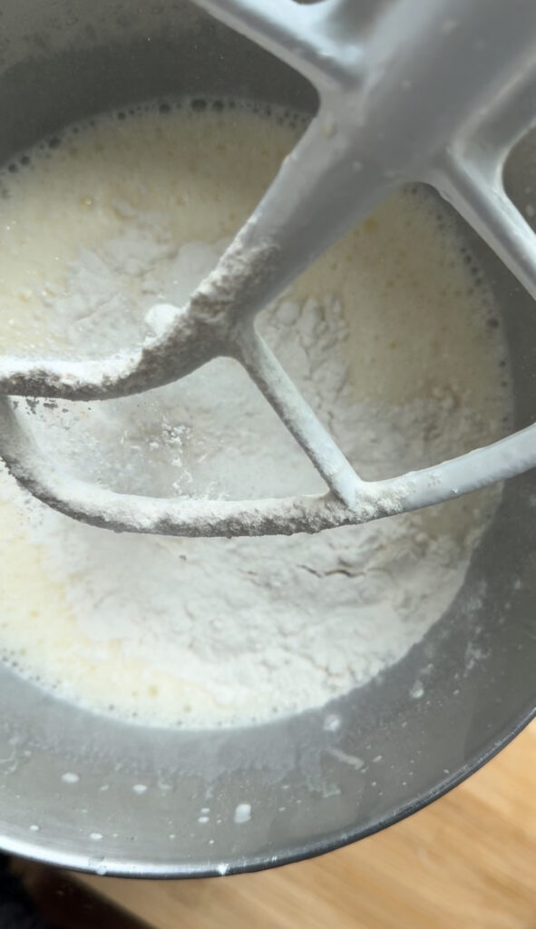 Adding flour to the the bowl of a stand mixer.