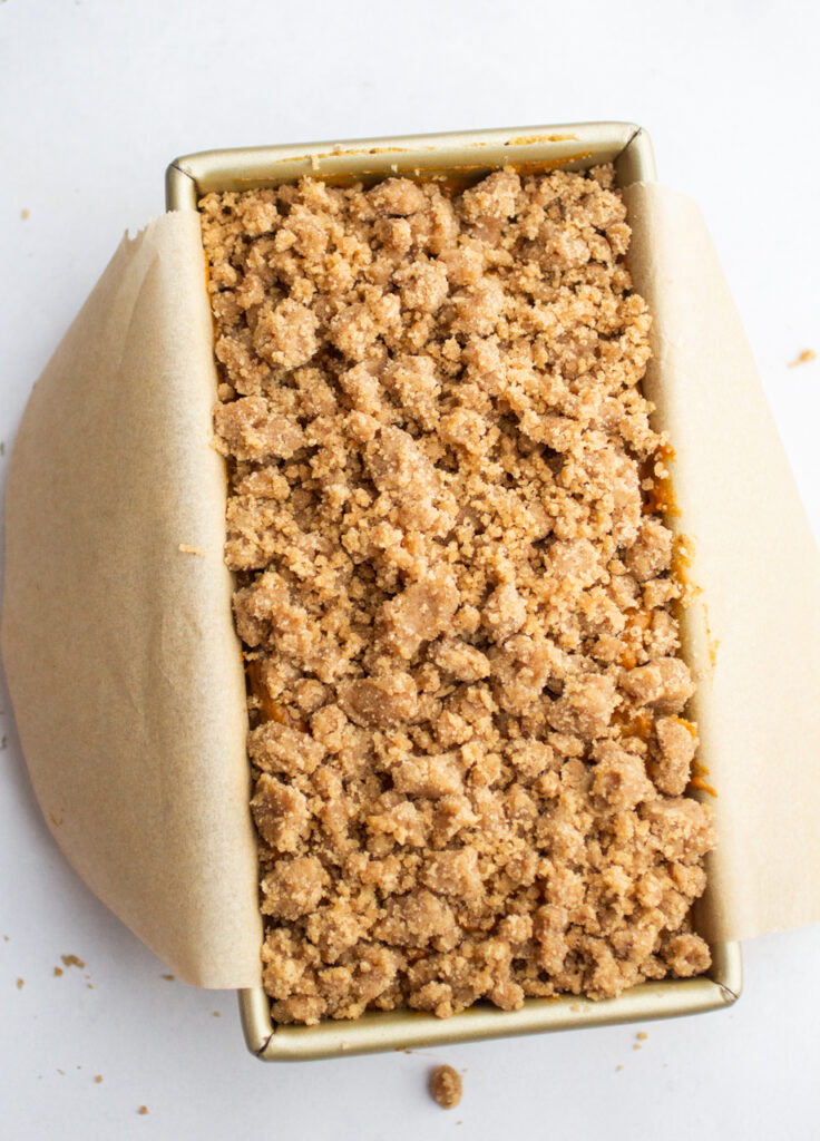 pumpkin bread batter topped with streusel in a parchment-lined loaf pan.