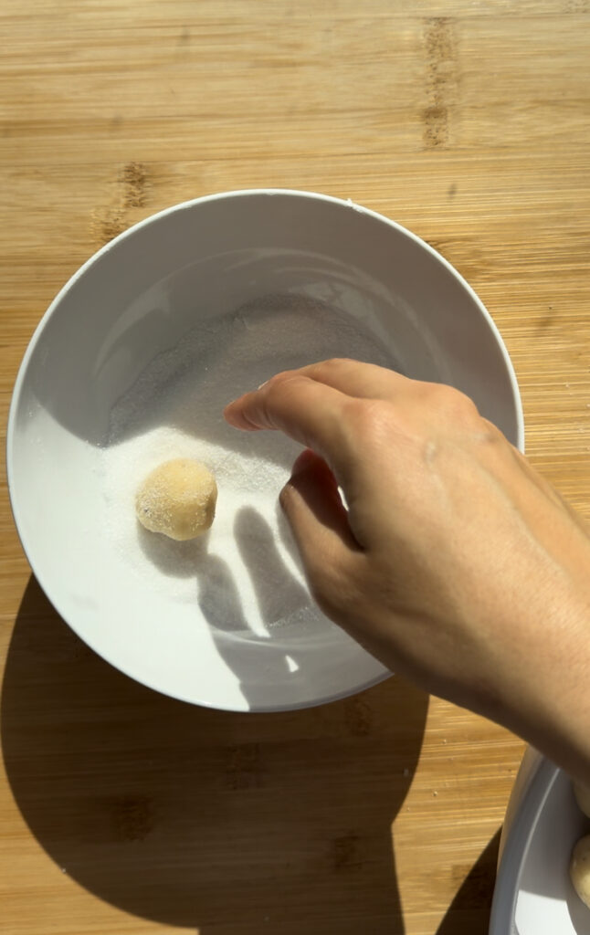 Rolling dough balls in a bowl of sugar.