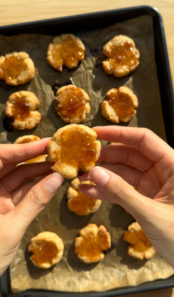 A cheese thumbprint cookie held by two hands.