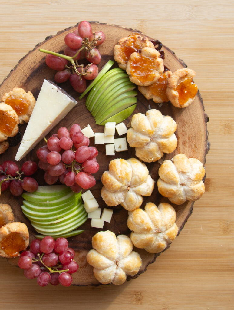 a cheeseboard with grapes, apples and pumpkin shaped brie bites.