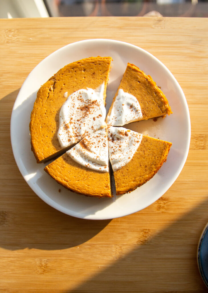 A sliced pumpkin cheesecake topped with yogurt and cinnamon on a white plate.