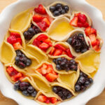 A white pie dish filled with mini red, yellow and blue hand pies.
